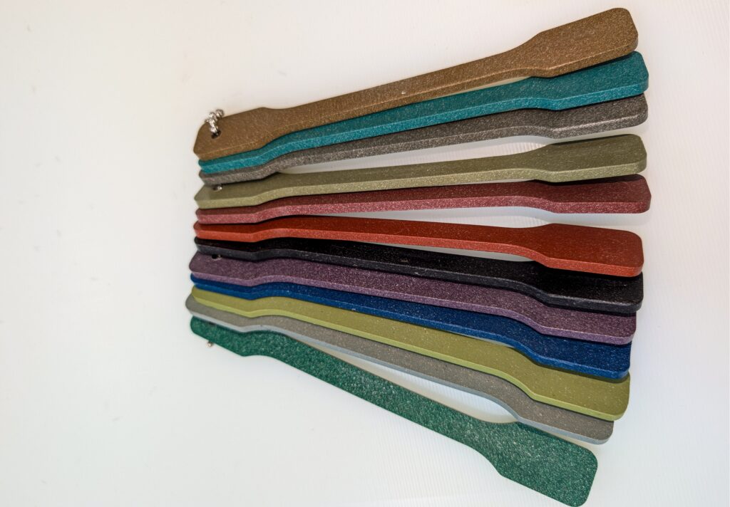 Muestrario en forma de paletas unidas por cadena con muestras texturizadas en varios colores (marrón, verde, gris, rojo, morado, azul).